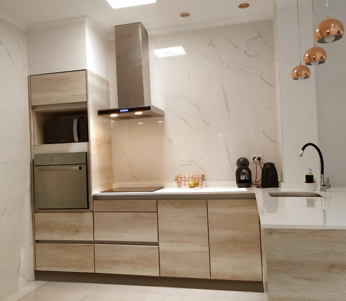 Cocina moderna remodelada por el estudio, con muebles de madera clara y revestimiento de mármol